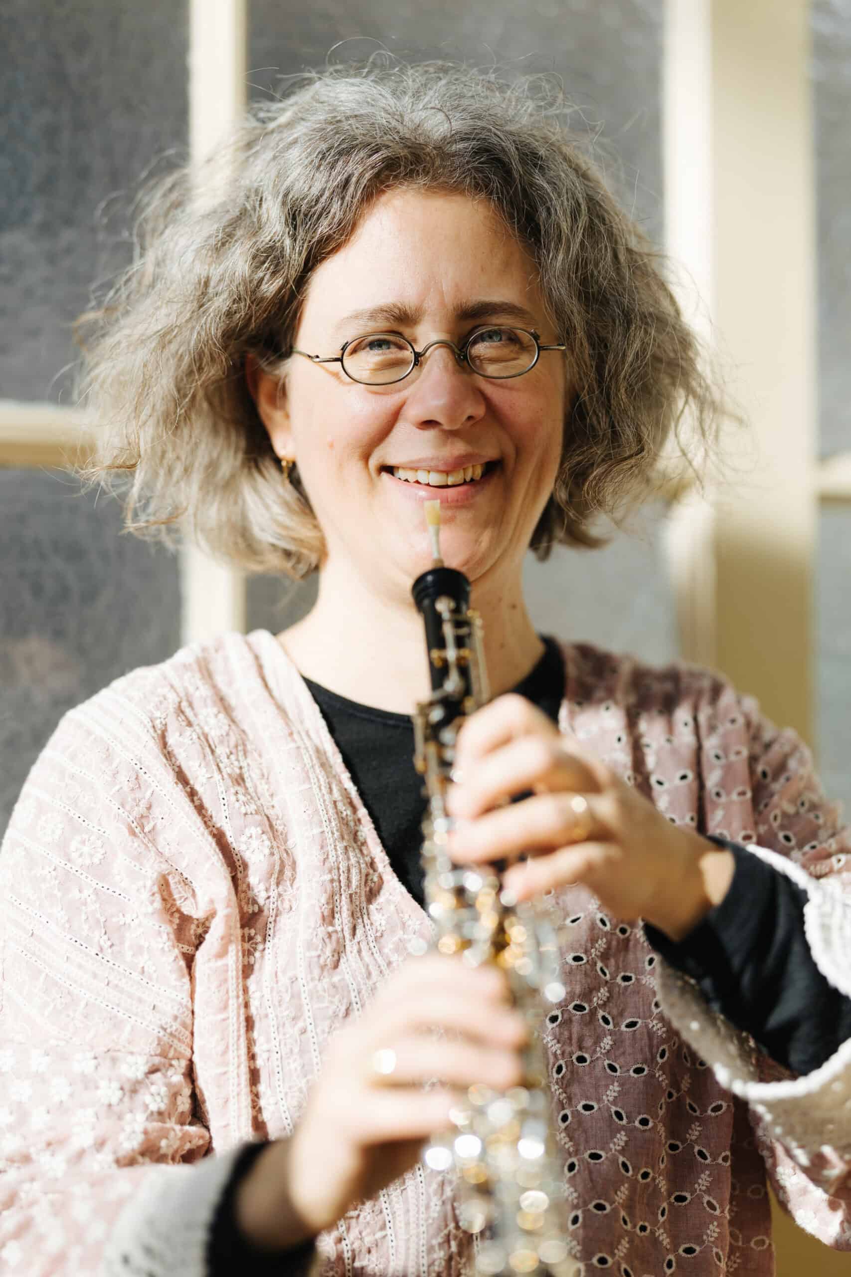 Eine lächelnde Person mit grauen Locken und Brille hält ein Holzblasinstrument, möglicherweise eine Oboe, in einem Raum in der Hand, während hinter ihr Sonnenlicht durch ein Fenster scheint – dieses Bild könnte gut als Begleitbild zu einer „Über mich“-Vorstellung dienen. Eine lächelnde Person mit grauen Locken und Brille hält ein Holzblasinstrument, möglicherweise eine Oboe, in einem Raum in der Hand, während hinter ihr Sonnenlicht durch ein Fenster scheint – dieses Bild könnte gut als Begleitbild zu einer „Über mich“-Vorstellung dienen.