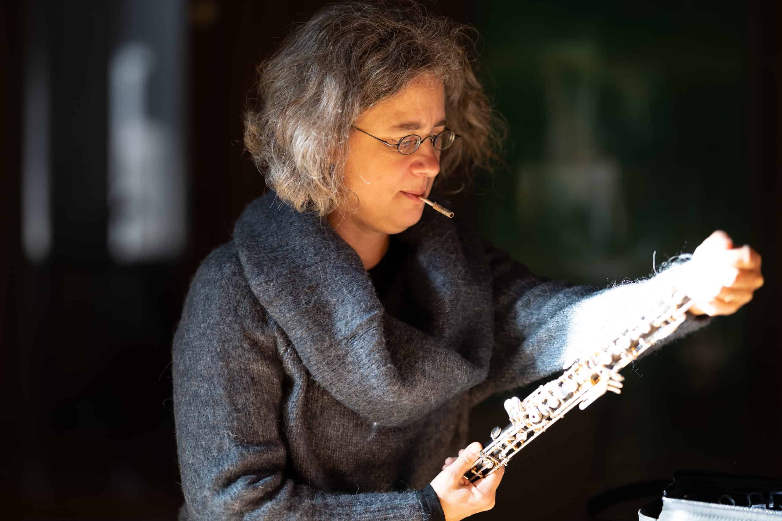 Eine Person mit lockigem Haar und Brille, die einen dicken grauen Pullover trägt, hält eine Oboe in der Hand und scheint diese mit einem kleinen Tuch im Mund zu reinigen – ein spontaner „Über mich“-Moment, eingefangen im Alltag. Eine Person mit lockigem Haar und Brille, die einen dicken grauen Pullover trägt, hält eine Oboe in der Hand und scheint diese mit einem kleinen Tuch im Mund zu reinigen – ein spontaner „Über mich“-Moment, eingefangen im Alltag.